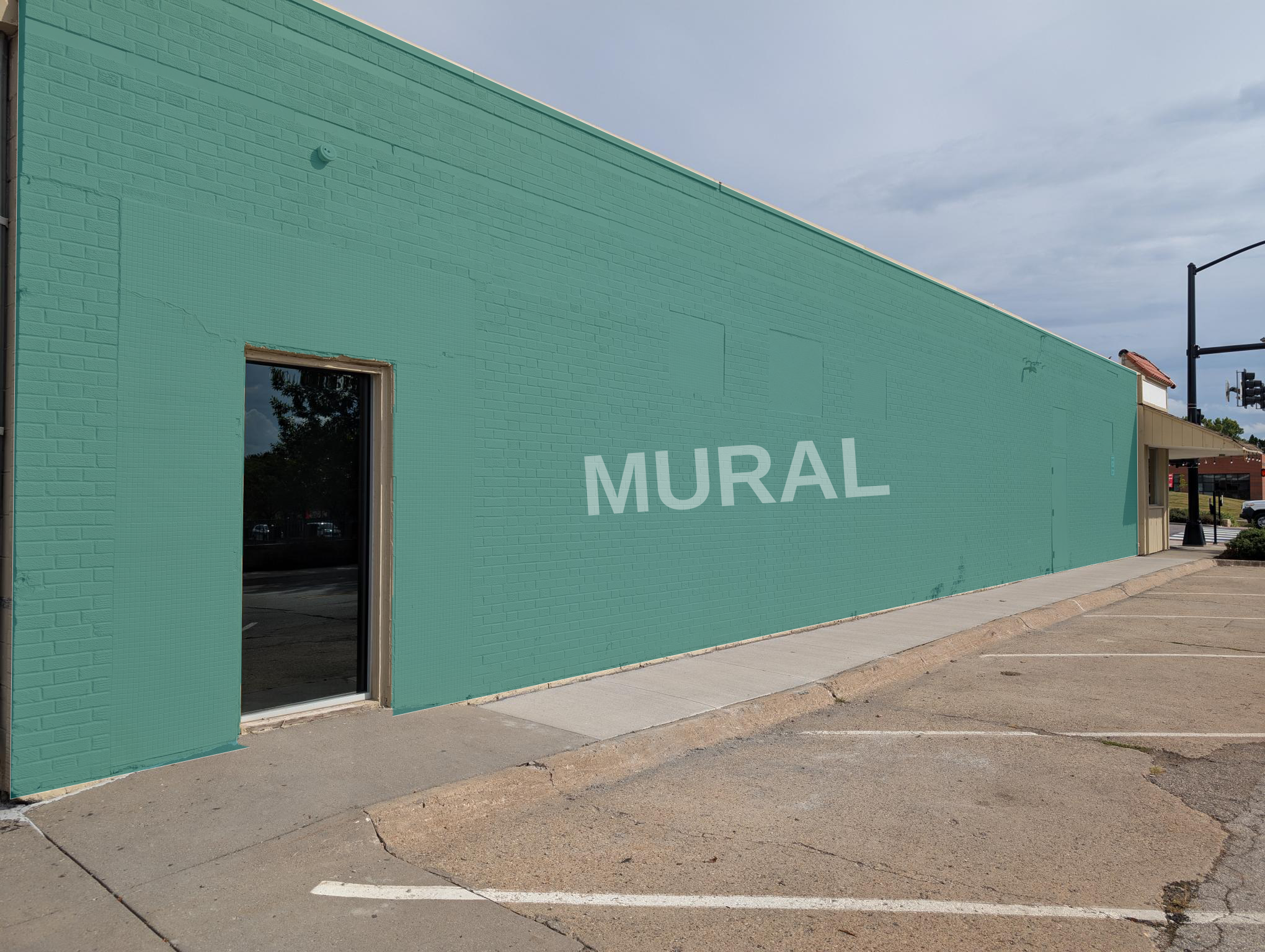 Long teal-painted brick wall labeled ‘MURAL’ along a sidewalk with a window on the left.