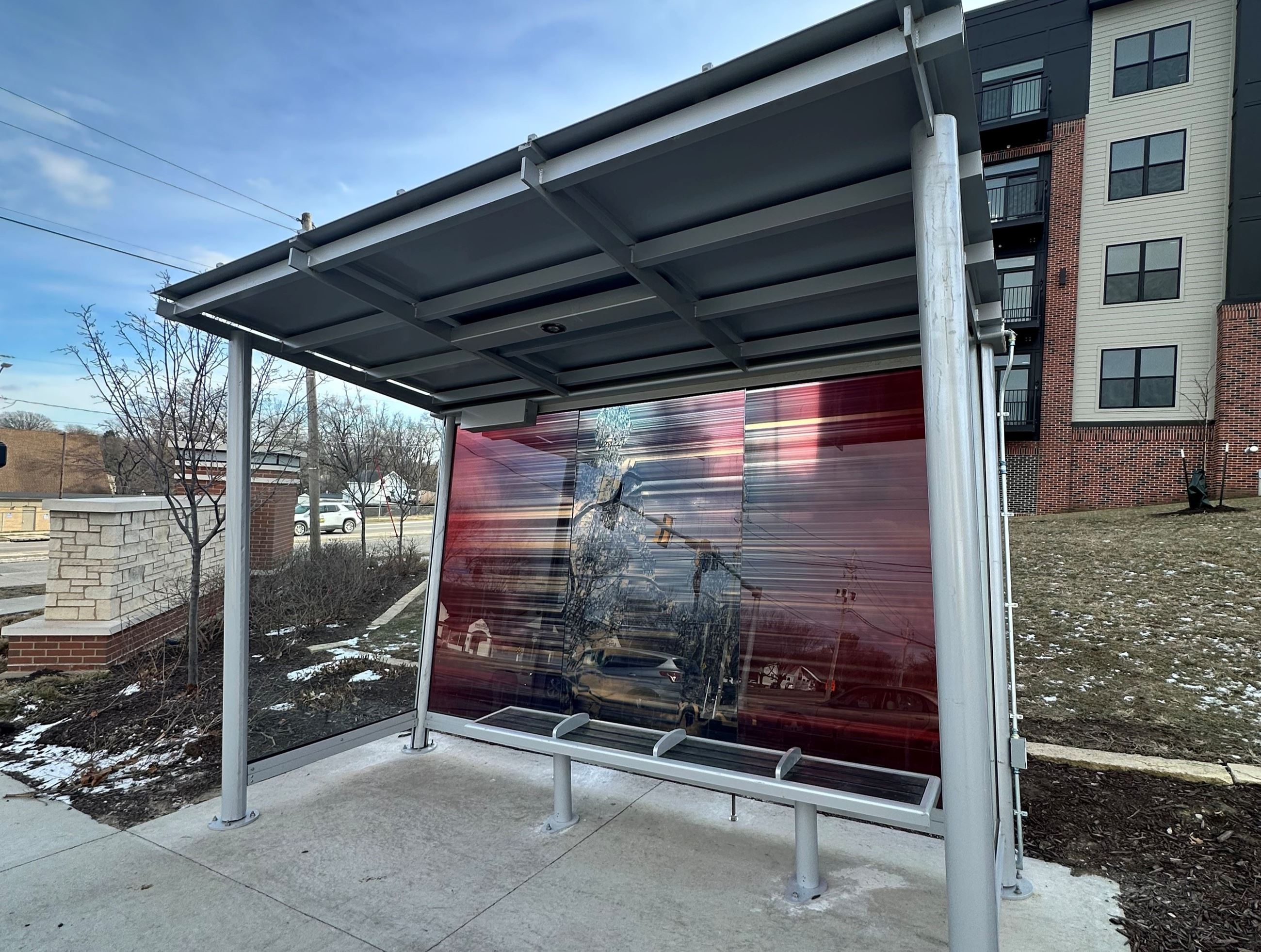 Modern bus shelter with red abstract glass art panel near apartments on a winter day